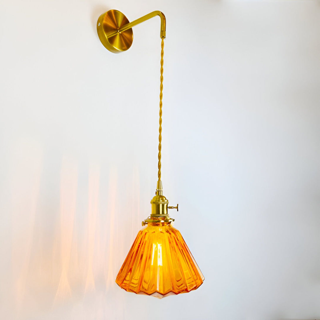 Une applique murale de style baroque avec une finition en laiton et un abat-jour en verre orange. L'applique est fixée au mur par une plaque ronde en laiton et est suspendue par un cordon en tissu torsadé doré. L'abat-jour est en forme de cloche et est fabriqué en verre orange texturé. L'applique est munie d'un interrupteur à bascule en laiton situé sur la plaque murale. SE-3306234591,SE-4665181012,SE-3669452133,
