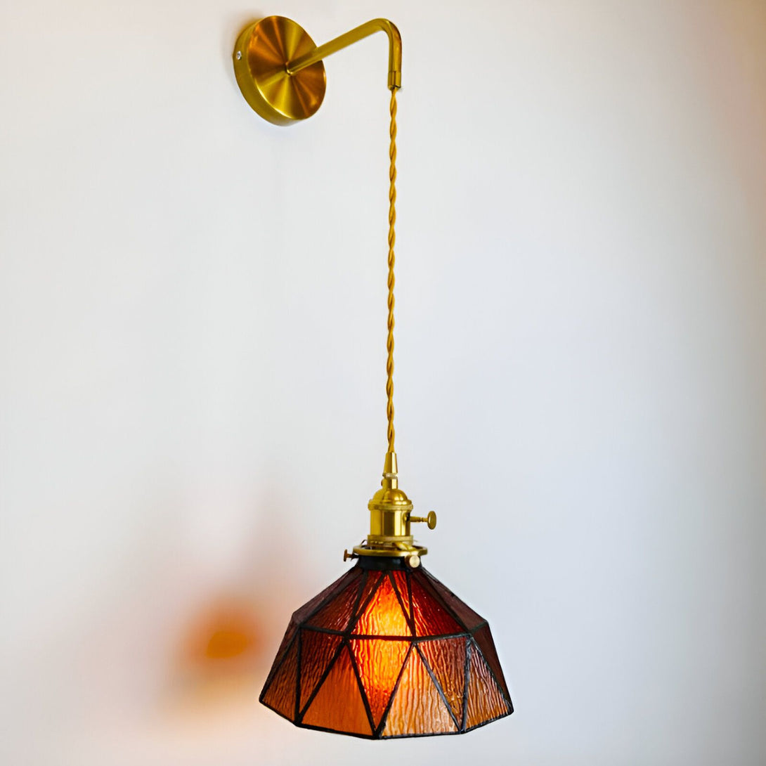 Une applique murale de style baroque avec une finition en laiton et un abat-jour en verre teinté de couleur ambre. L'applique est fixée au mur par une plaque ronde en laiton et est suspendue par une chaîne en laiton. L'abat-jour est de forme géométrique et est composé de plusieurs morceaux de verre teinté de couleur ambre. L'applique est éclairée par une ampoule à incandescence. SE-3306234591,SE-4665181012,SE-3669452133,