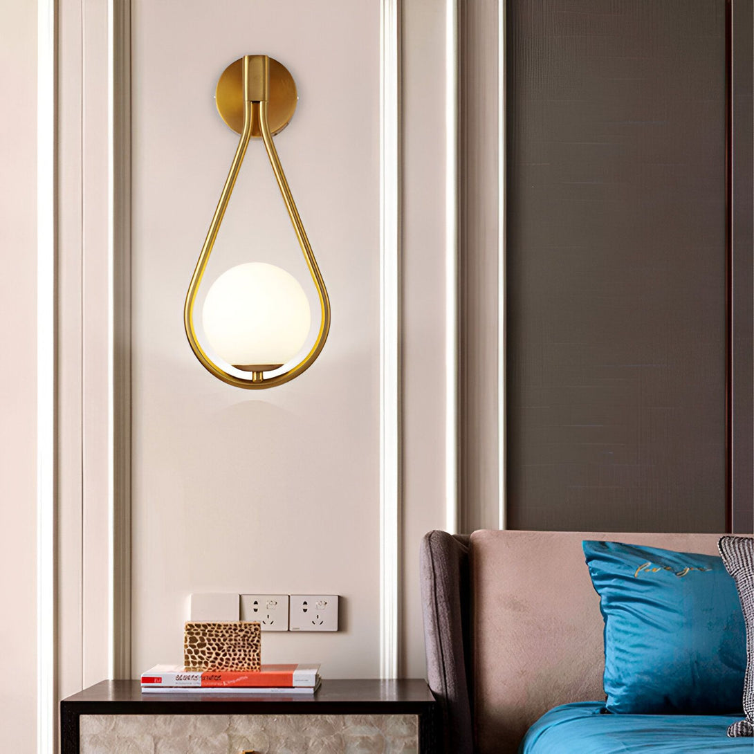 Une applique murale en forme de larme avec une finition dorée. L'abat-jour est en verre opale blanc. L'applique est fixée au mur par une plaque ronde en métal doré. RE-3583298055,
