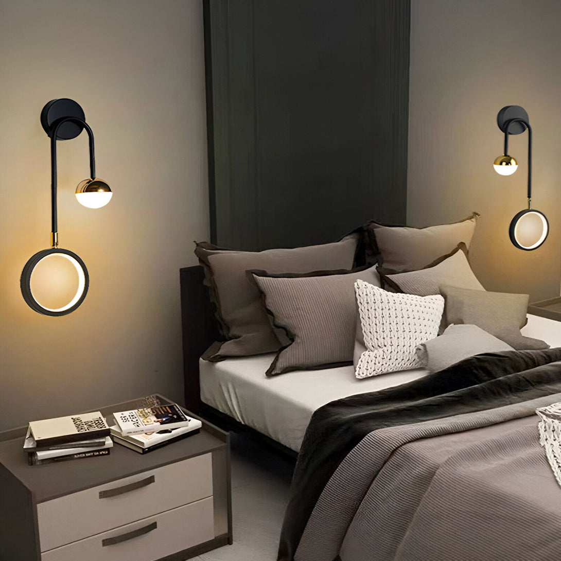 Une paire d'élégantes appliques murales noires et dorées. Elles sont toutes les deux composées d'un globe doré et d'un anneau lumineux blanc. Les appliques sont fixées au mur au-dessus d'un lit. SI-404465915X,SI-9313062666,SI-8244315253,SI-2796814408,SI-4937030671,SI-7340808590,SI-742479745X,SI-8530495985,SI-6643510554,SI-3922651682,SI-5308641021,SI-222868936X,