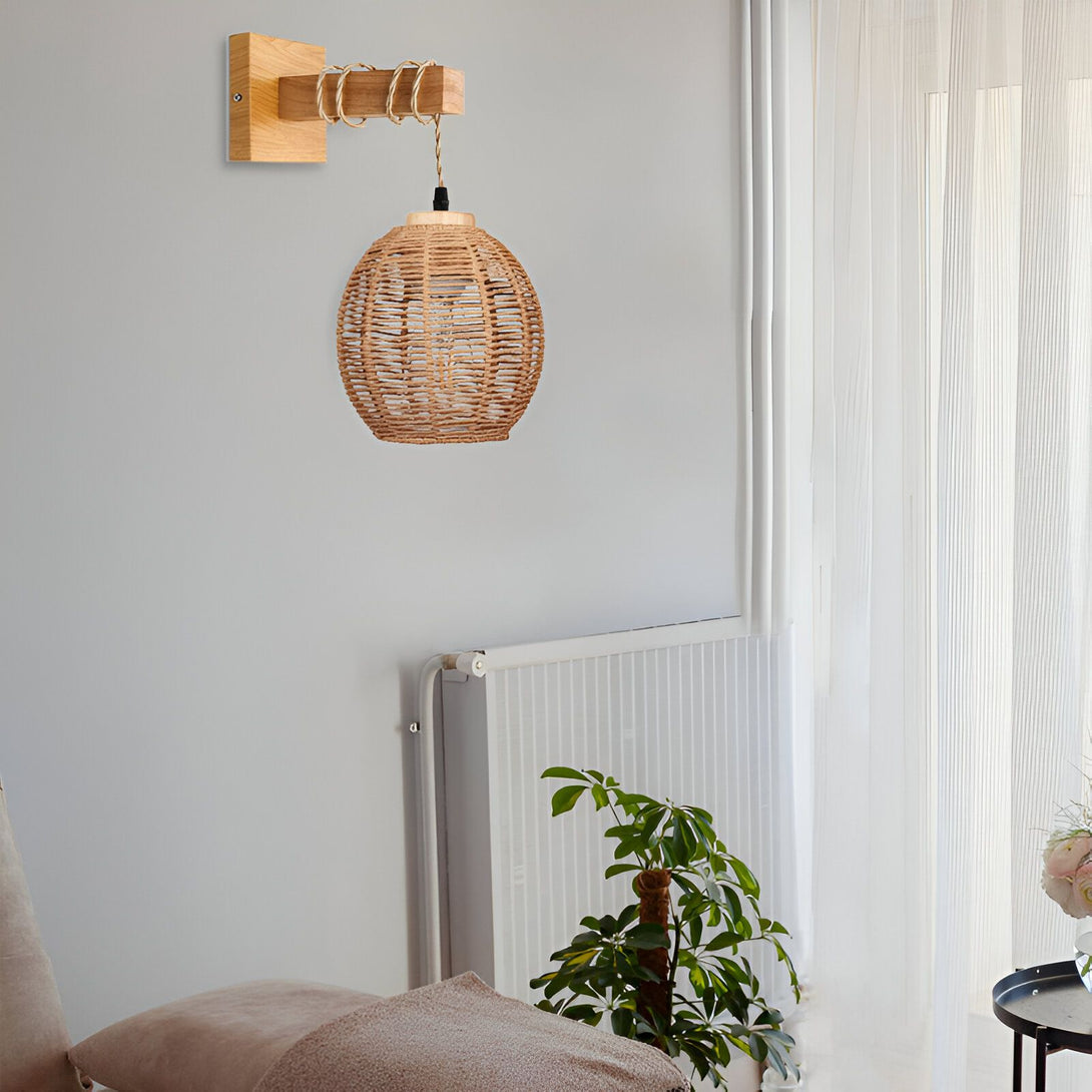 Une applique murale en bois avec une corde et une abat-jour en osier tressé. À côté, se trouve un radiateur et une plante verte. ER-557575426X,