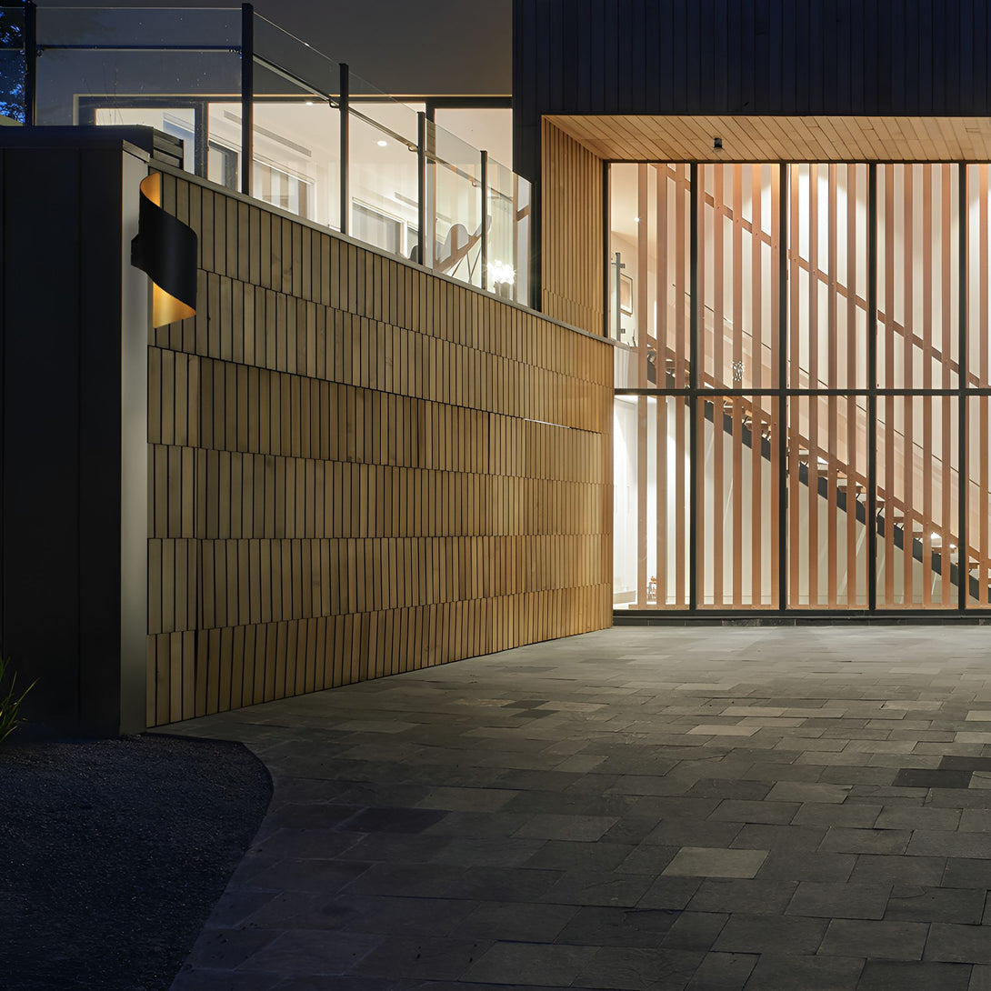 Une image d'une maison moderne avec une porte de garage en bois et une allée en pierre. La maison est éclairée par une lampe noire et il y a des plantes vertes dans le jardin. LI-469870085X,LI-0368927849,