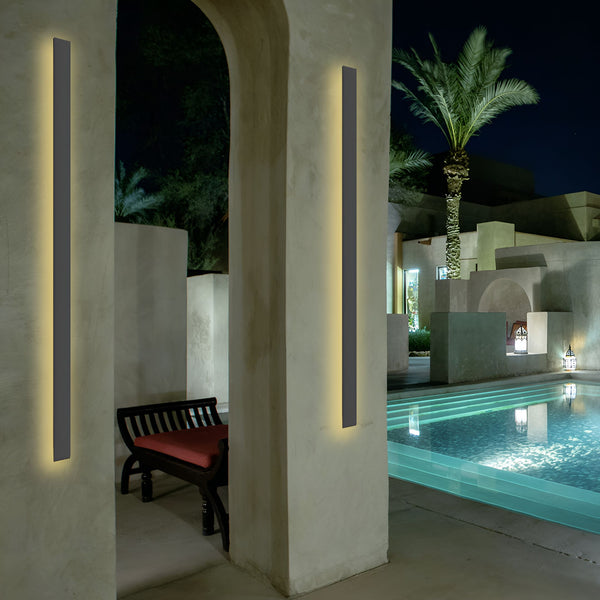 Deux appliques murales noires sont installées de chaque côté d'une porte. Les appliques sont rectangulaires et émettent une lumière blanche. La porte est ouverte et donne sur une terrasse avec une piscine. Il y a un palmier et des lanternes sur la terrasse. AM-2720633216,AM-3830779852,AM-618964516X,
