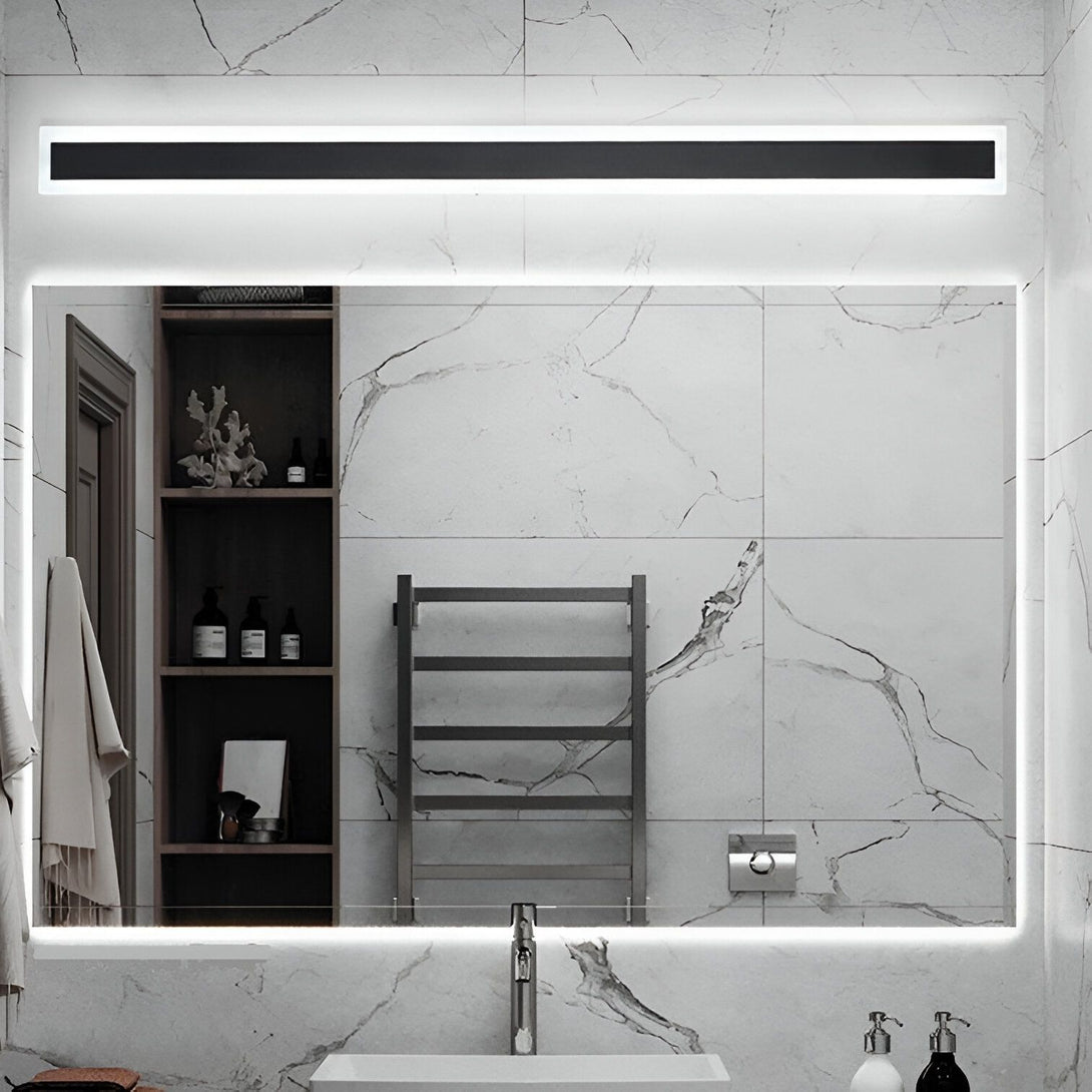Une salle de bain avec un grand miroir éclairé par une lumière LED au-dessus. Il y a une étagère ouverte sur le côté gauche du miroir avec des produits de beauté dessus. Il y a aussi un sèche-serviettes noir à droite du miroir. Le sol est en marbre blanc. AM-2720633216,AM-3830779852,AM-618964516X,