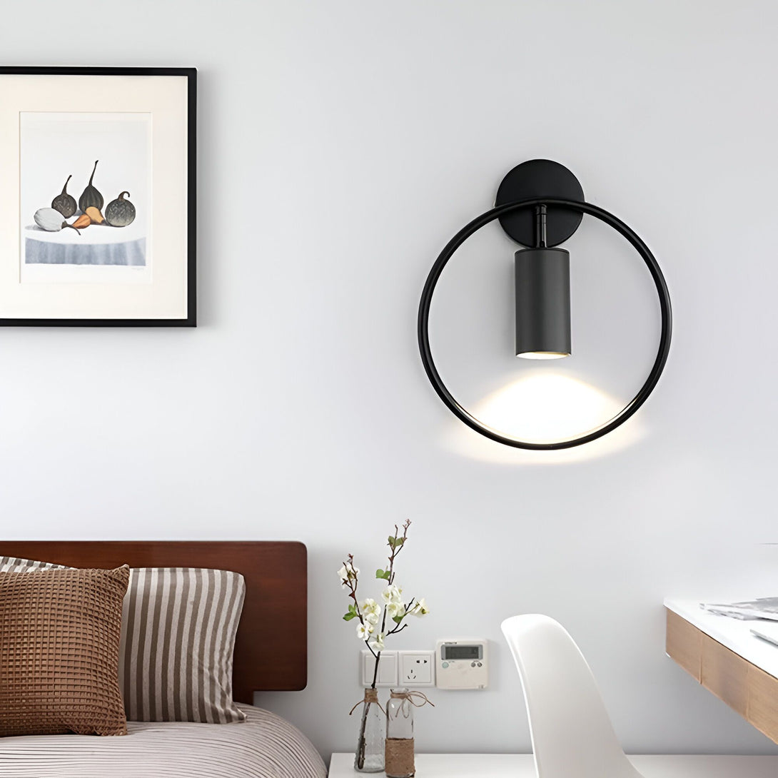 Une image d'une applique murale noire en forme de cercle. L'applique est fixée au mur et émet une lumière blanche. À côté de l'applique, il y a un cadre avec une image en noir et blanc. ME-509545663X,ME-2239075813,ME-9122701958,