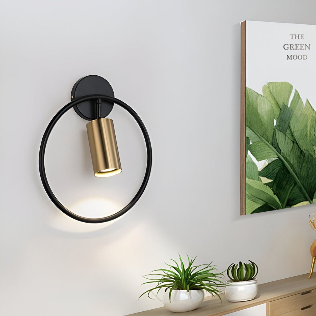 Une applique murale noire avec un anneau doré et une lumière dorée qui brille. À côté, il y a un cadre avec une image de feuilles vertes. ME-509545663X,ME-2239075813,ME-9122701958,