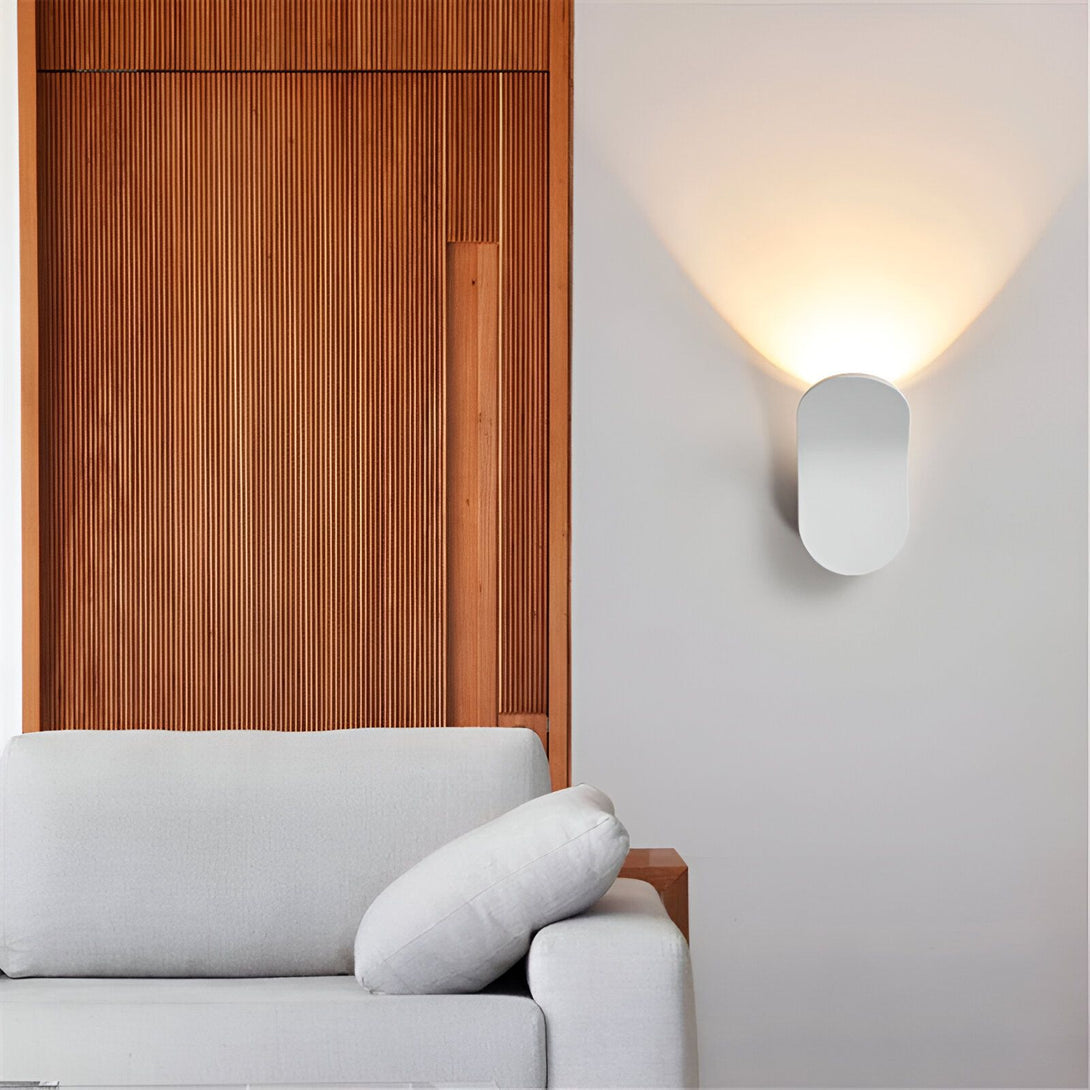 Une image d'une applique murale blanche de forme ovale émettant une lumière chaude sur un mur blanc à côté d'un canapé gris et d'une porte en bois. DE-8054556632,DE-0853481989,DE-2502387817,DE-7283470557,DE-6011146961,DE-3639032594,DE-4151317678,DE-0168772612,DE-6626641387,DE-2260219322,DE-6307227001,DE-3738266372,DE-8511010173,DE-7036764996,DE-4587051241,DE-9018460893,DE-0632344601,DE-4256653104,DE-5000257235,DE-4700066563,DE-3834710490,