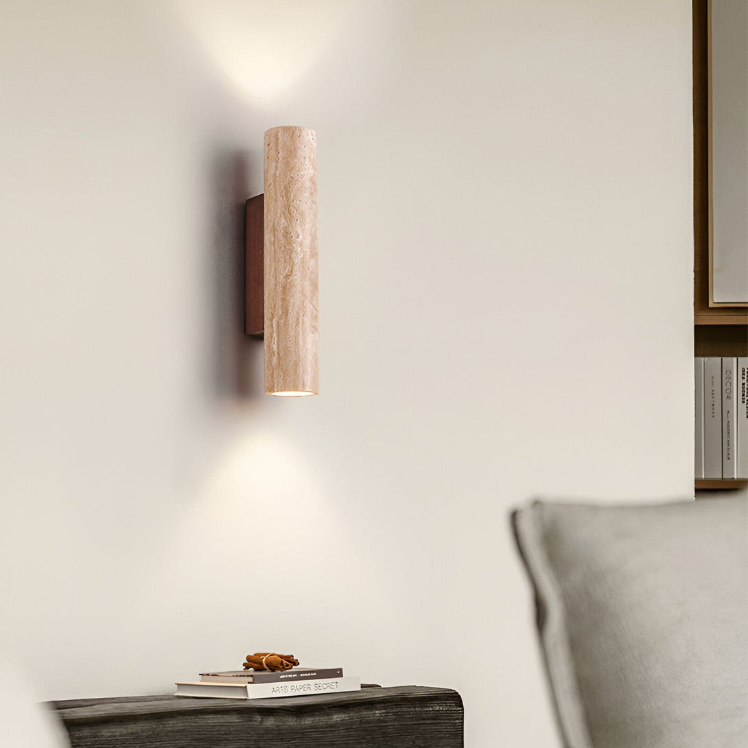 Une applique murale en marbre beige et métal marron est fixée au mur. Elle diffuse une lumière chaude et tamisée. À côté, se trouve une table en bois avec un livre et des objets de décoration. ME-6043674122,