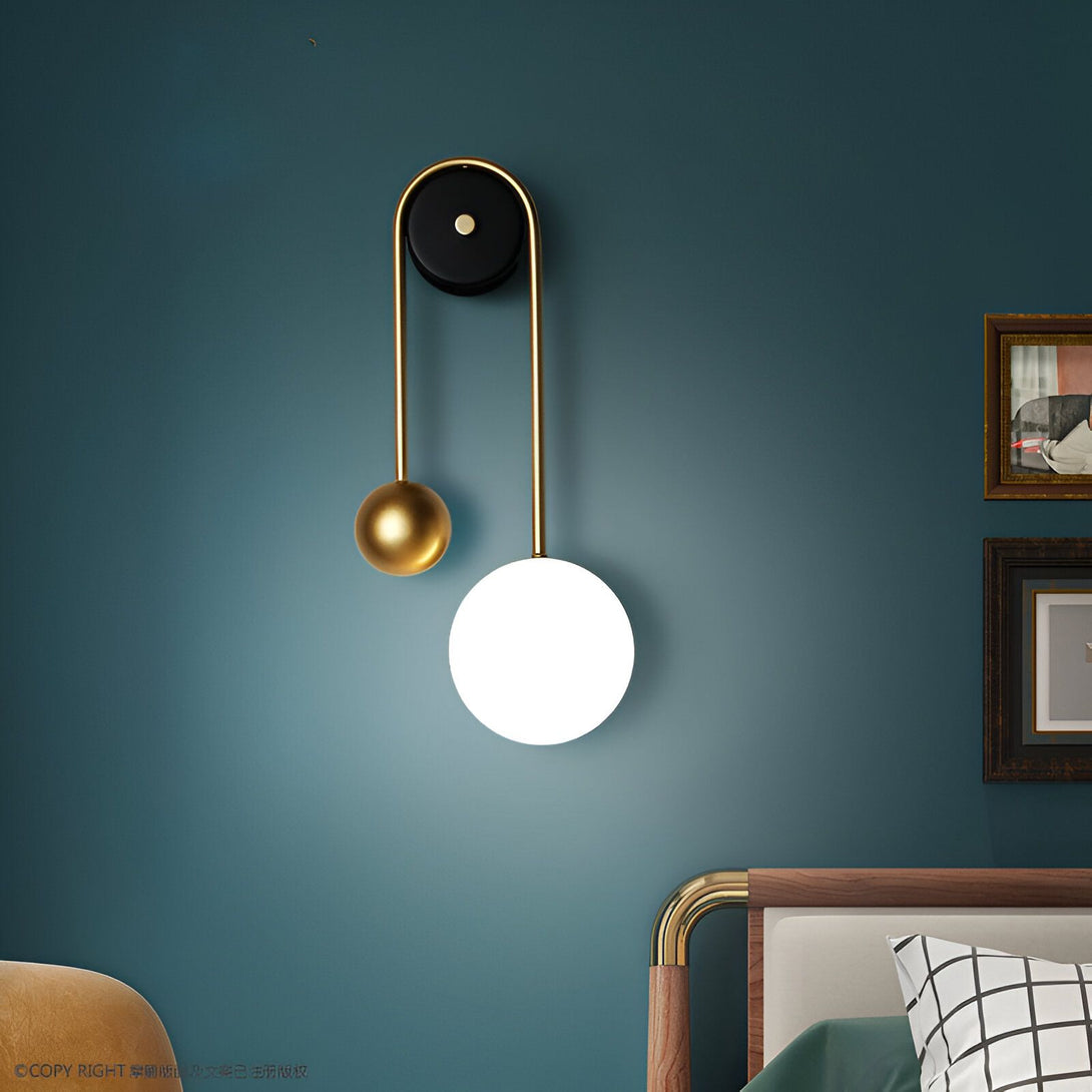 Une applique murale avec une sphère en verre blanc et une petite sphère en métal doré. L'applique est fixée au mur par un fil noir. MI-5508556966,