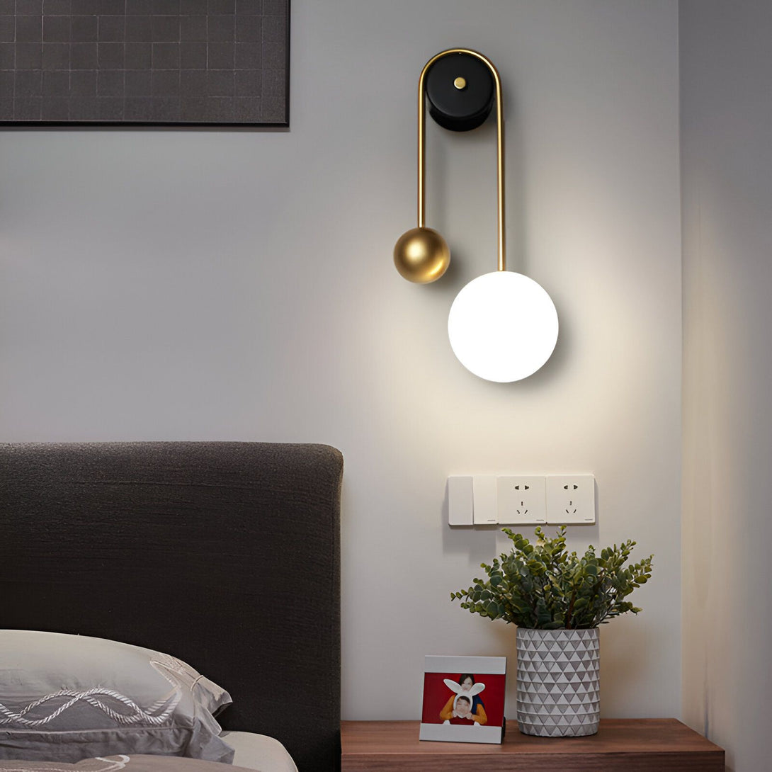 Une applique murale avec une sphère en verre blanc et une sphère en métal doré. L'applique est fixée au mur par un support noir. MI-5508556966,