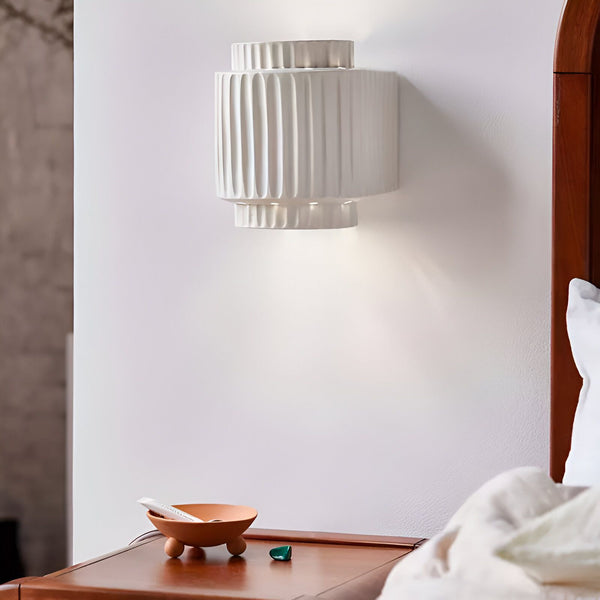 Une applique murale blanche en céramique texturée est fixée au mur au-dessus d'une table de chevet en bois. Sur la table de chevet se trouvent un bol en céramique contenant un tube de crème solaire et un petit cristal vert. DE-2211618871,DE-9387341801,