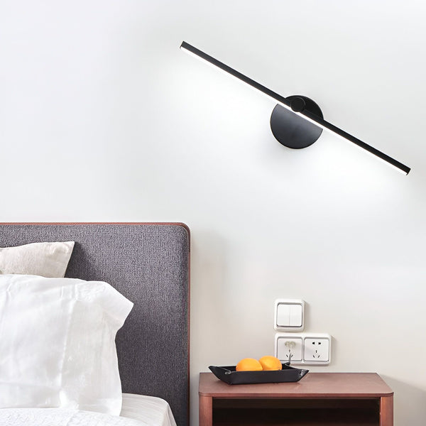 Une image d'une applique murale noire avec une lumière blanche. L'applique est fixée au mur au-dessus d'un lit avec une tête de lit grise. Il y a une table de chevet en bois à côté du lit avec un plateau dessus avec deux oranges. ME-6834158499,ME-298807044X,ME-9594073322,ME-5425764731,ME-4242394632,ME-8956104360,ME-6143226717,ME-8366071057,ME-6572957039,ME-7723649002,ME-2300392488,ME-4531599233,ME-2192844751,ME-7933107605,ME-947367516X,ME-0064659658,ME-6794960591,ME-1580687326,