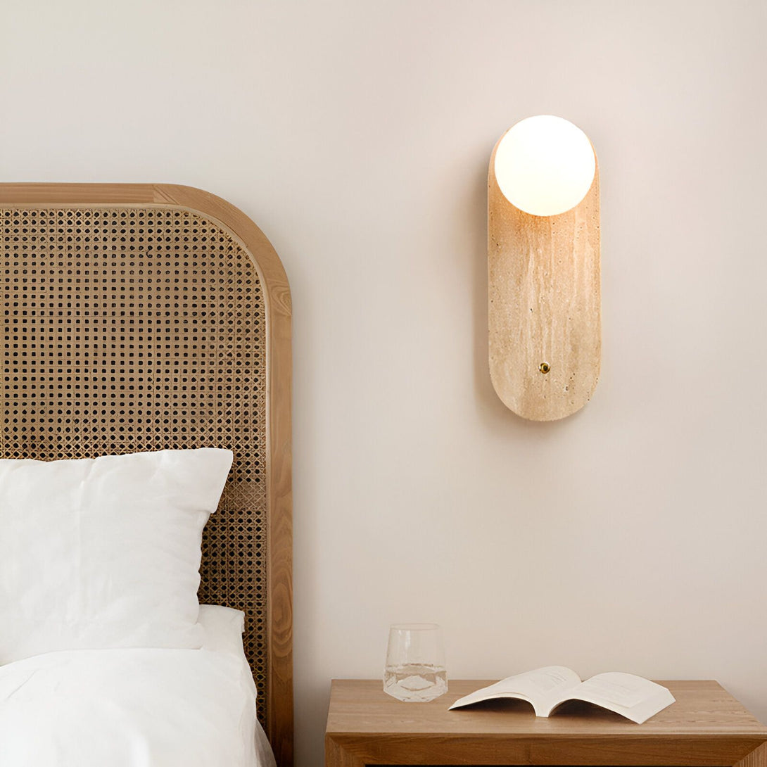 Une image d'une applique murale en pierre avec une lumière blanche chaude. L'applique est montée sur un mur beige et est située à côté d'un lit avec une tête de lit en rotin. Sur la table de chevet, il y a un verre d'eau et un livre ouvert. HO-6953652675,HO-8029463928,