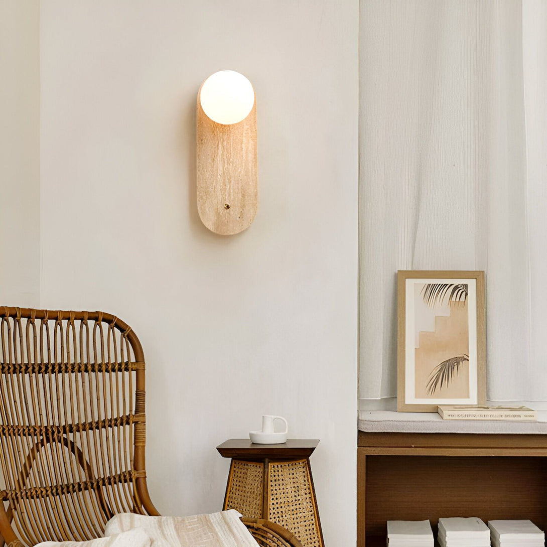 Une applique murale en bois avec une forme ovale et une lumière blanche. À côté, il y a une chaise en osier et une table en osier avec une bougie dessus. Il y a aussi un cadre avec une image de feuilles de palmier. HO-6953652675,HO-8029463928,
