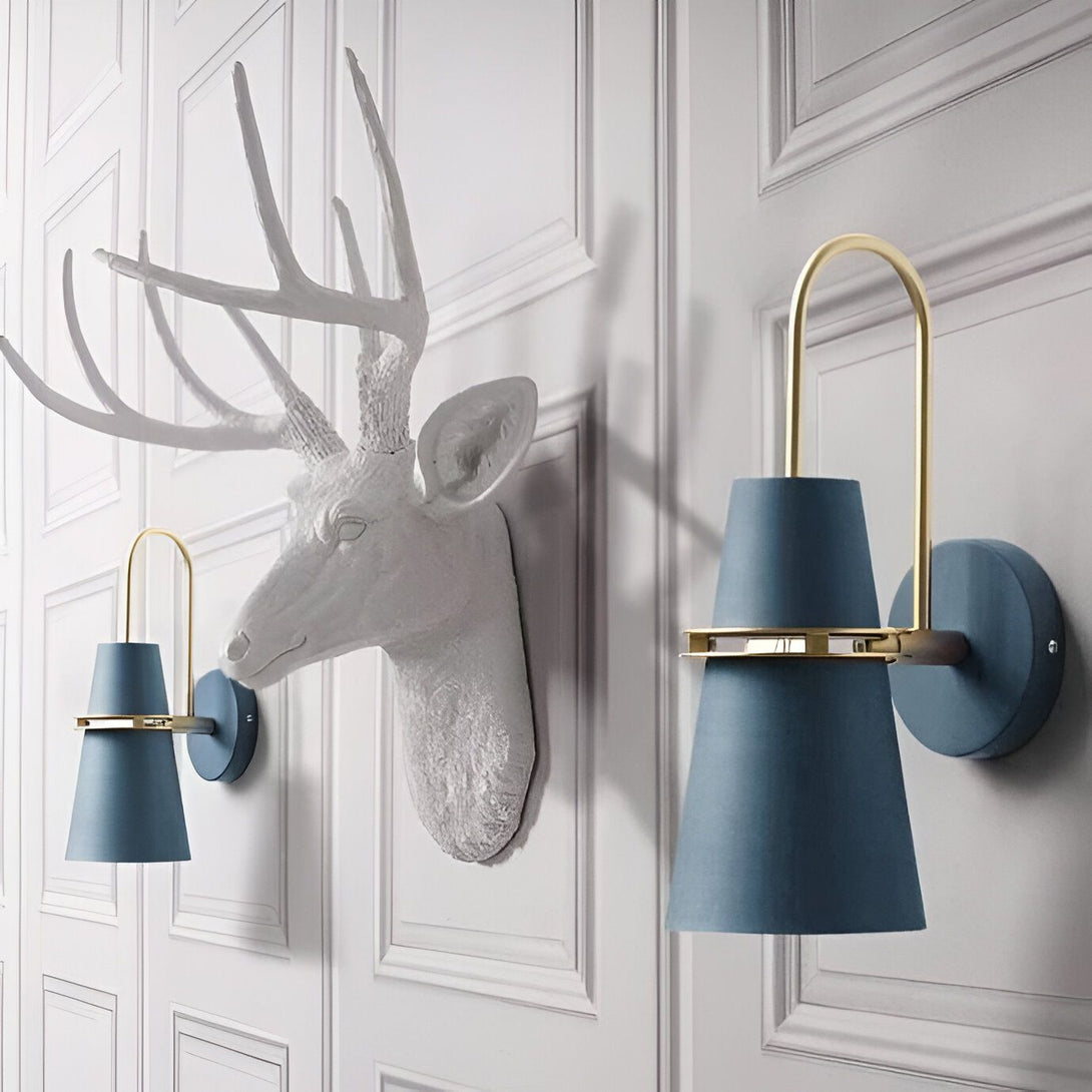 Une paire d'appliques murales en forme de cône bleu avec des détails dorés. Les appliques sont fixées à un mur blanc à côté d'une tête de cerf en résine. KA-4033461906,KA-553605905X,KA-6540244266,