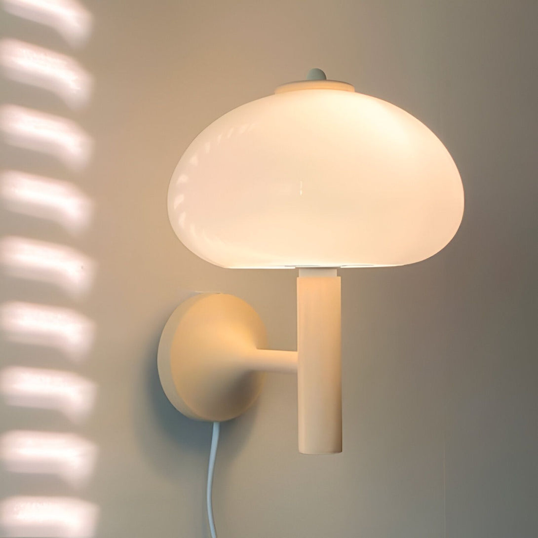 Une applique murale blanche en forme de champignon est fixée au mur. La lumière est allumée et projette des ombres sur le mur. JA-4181874648,
