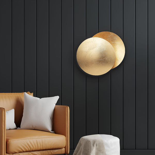 Une image d'un mur en bois noir avec une applique murale en forme de disque doré. À côté du mur, il y a un canapé en cuir marron avec des coussins blancs. EC-2203444304,EC-1181518121,EC-1128189976,EC-4141118907,