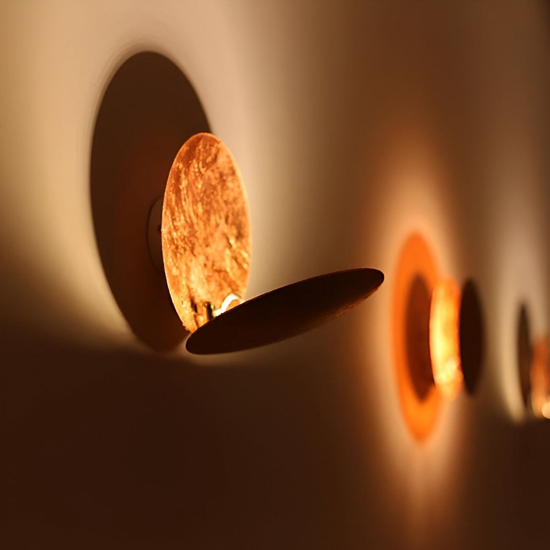 Une image d'une applique murale en cuivre. L'applique est ronde et a une forme de disque. Elle est fixée au mur par un petit support rond. La lumière est allumée et projette une ombre ronde sur le mur. EC-2203444304,EC-1181518121,EC-1128189976,EC-4141118907,