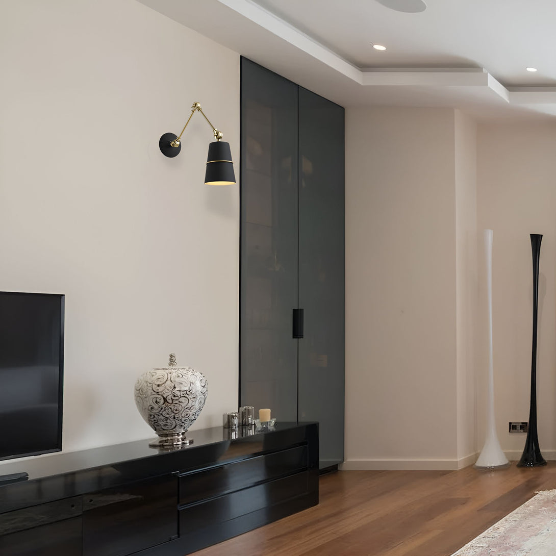 Une image d'une applique murale noire avec un abat-jour en laiton. L'applique est fixée à un mur blanc et est située à côté d'une porte noire. Il y a une télévision et un meuble TV noir en dessous de l'applique. Il y a aussi un vase sur le meuble TV. Le sol est en bois et il y a un tapis au sol. AN-8444881139,AN-5410978560,