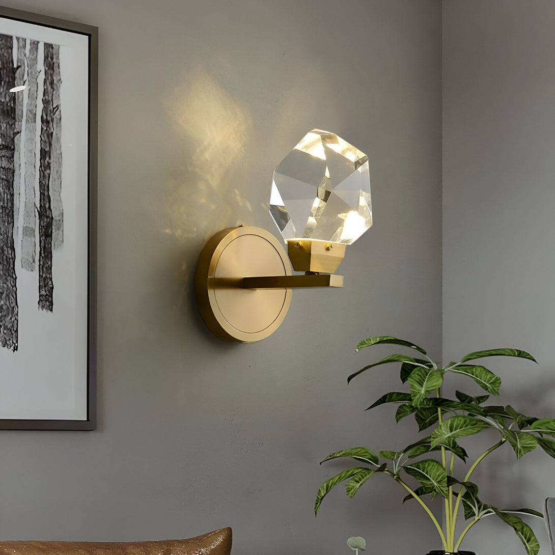 Une applique murale en laiton avec un abat-jour en cristal. L'applique est montée sur un mur gris et est entourée d'une plante verte. OP-5554030025,OP-6981510057,