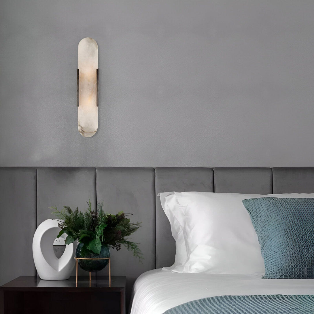 Une applique murale en albâtre et métal est fixée au mur au-dessus d'une table de chevet. Sur la table de chevet se trouve un vase en verre contenant des fleurs. FU-8330655202,FU-7846624369,FU-6574596262,FU-5000429826,