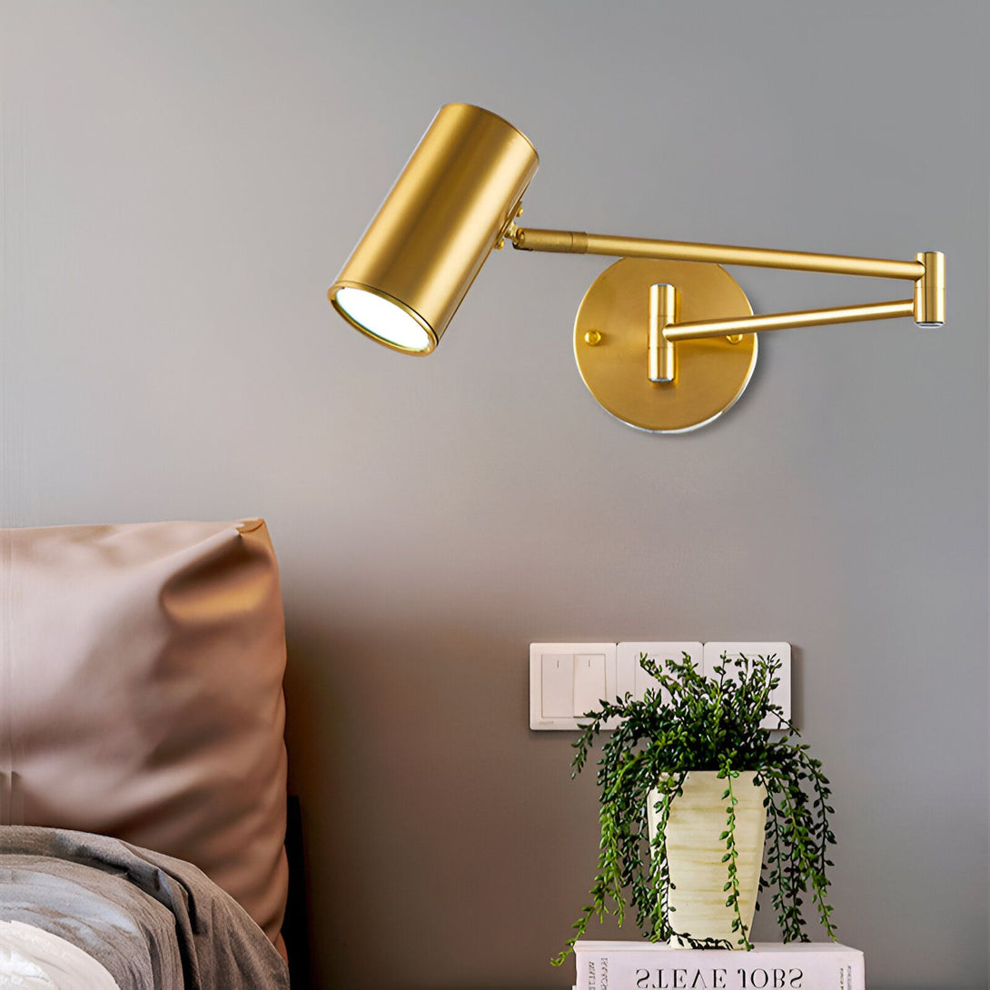 Une applique murale en laiton avec un abat-jour doré et un bras articulé. L'applique est fixée au mur au-dessus d'un lit. DE-9128165098,DE-7370131335,