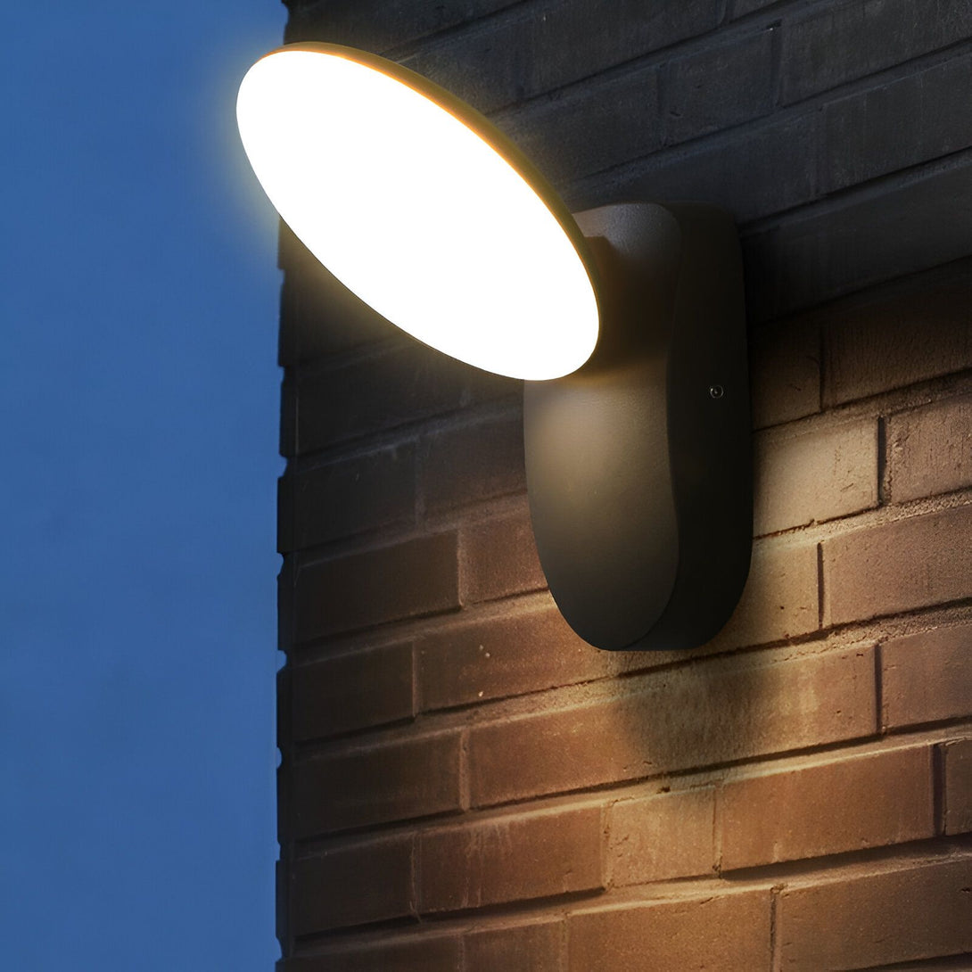 Une applique murale d'extérieur étanche de forme ronde et de couleur noire. L'applique est en aluminium et diffuse une lumière blanche et chaude. Elle est idéale pour éclairer une terrasse, un balcon ou une allée. LI-7997035176,LI-6815012948,