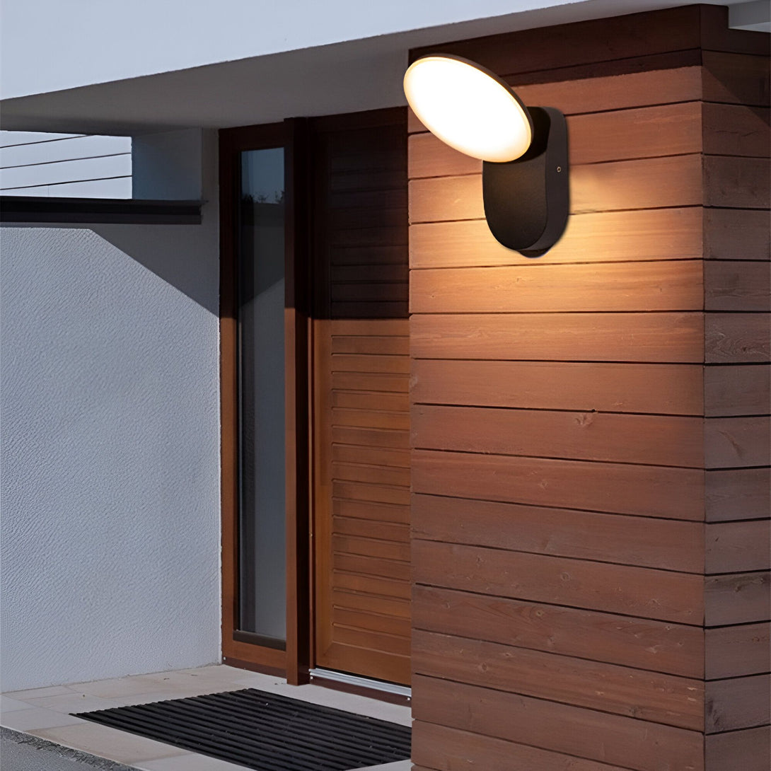 Une applique murale extérieure noire avec une forme ovale et une lumière blanche. L'applique est fixée sur un mur en bois. LI-7997035176,LI-6815012948,