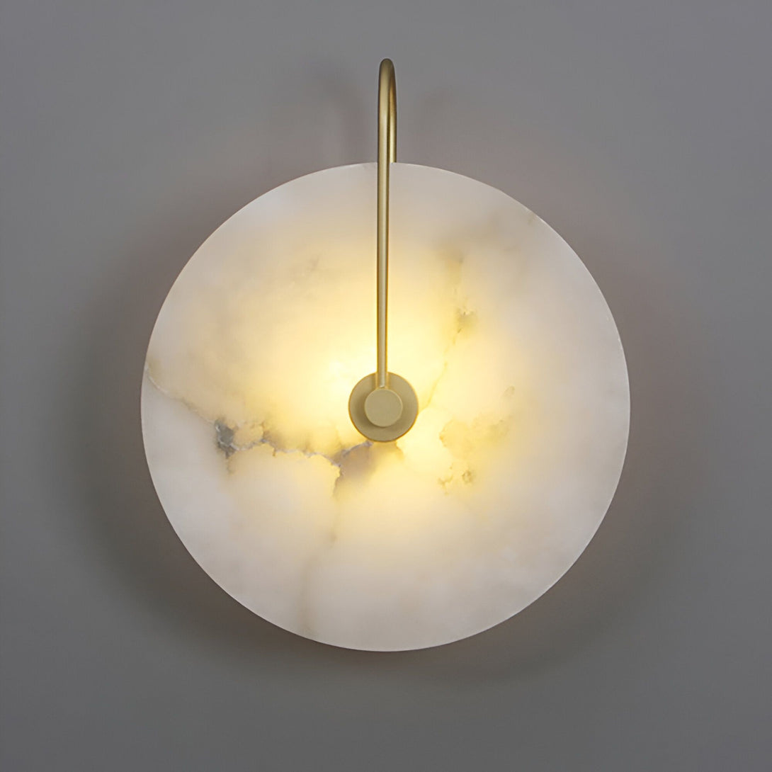 Une applique murale ronde en albâtre avec une bordure en laiton. La lumière est allumée et diffuse une lumière douce et chaude. NA-4097404784,NA-2974006701,NA-832145366X,NA-8668627538,