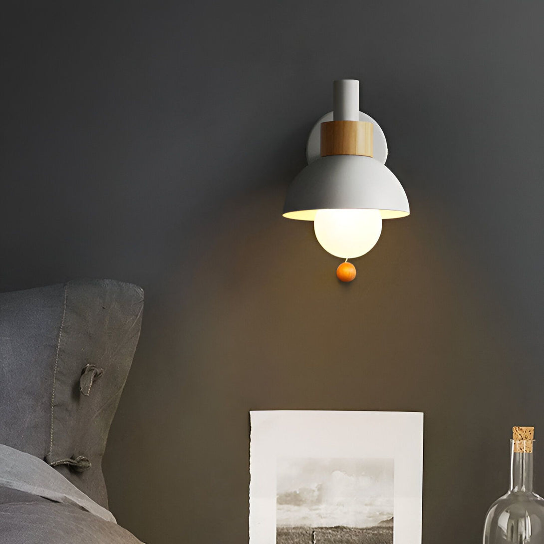 Une applique murale en métal gris avec un abat-jour en verre blanc et une tirette en bois. L'applique est montée sur un mur gris foncé et est allumée, ce qui projette une lumière chaude et diffuse dans la pièce. CU-0994507933,CU-6034342961,CU-307088881X,CU-4880091847,CU-0283329386,CU-3398585787,CU-2087585903,CU-7230351375,