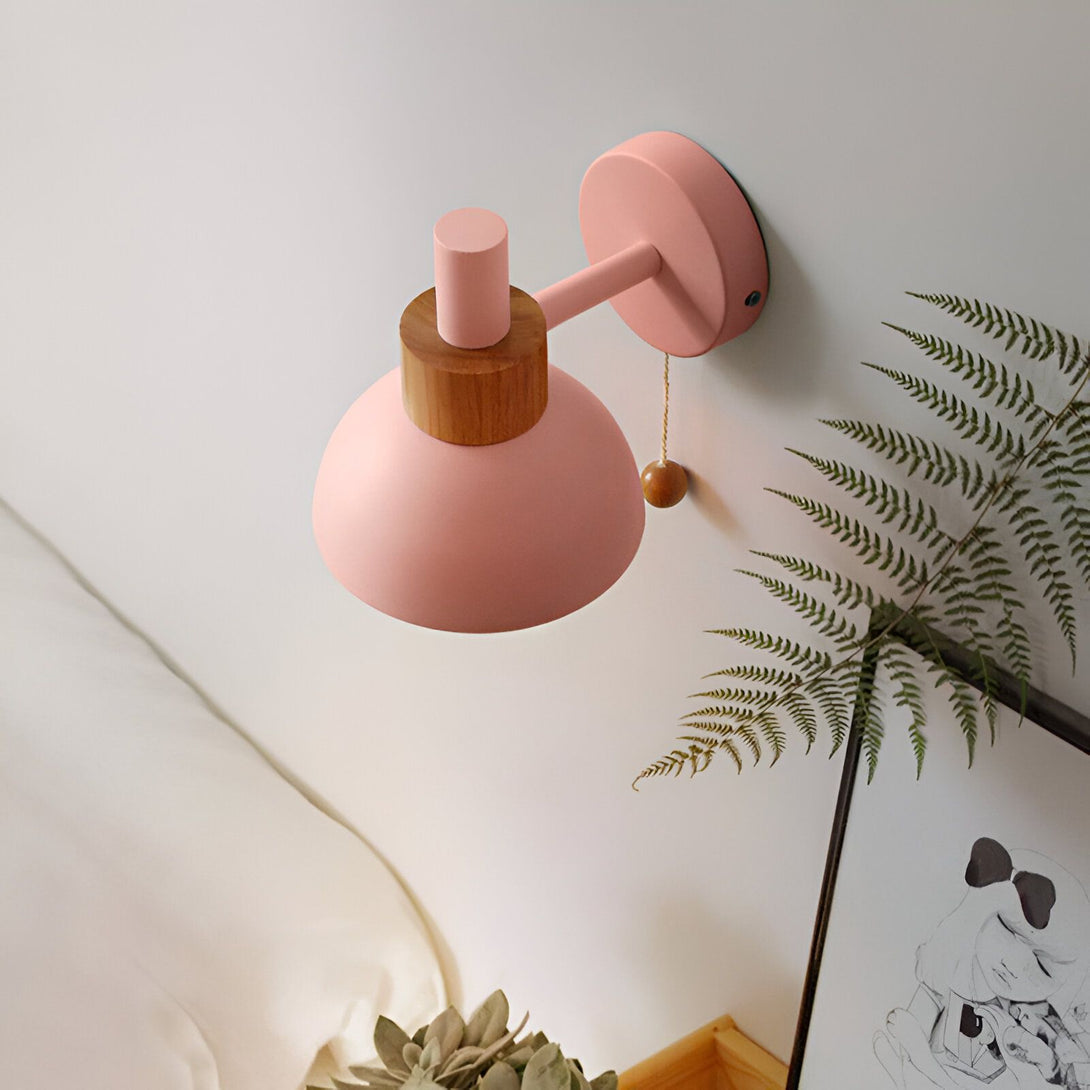 Une applique murale rose avec un abat-jour rond en métal et un interrupteur en bois. CU-0994507933,CU-6034342961,CU-307088881X,CU-4880091847,CU-0283329386,CU-3398585787,CU-2087585903,CU-7230351375,