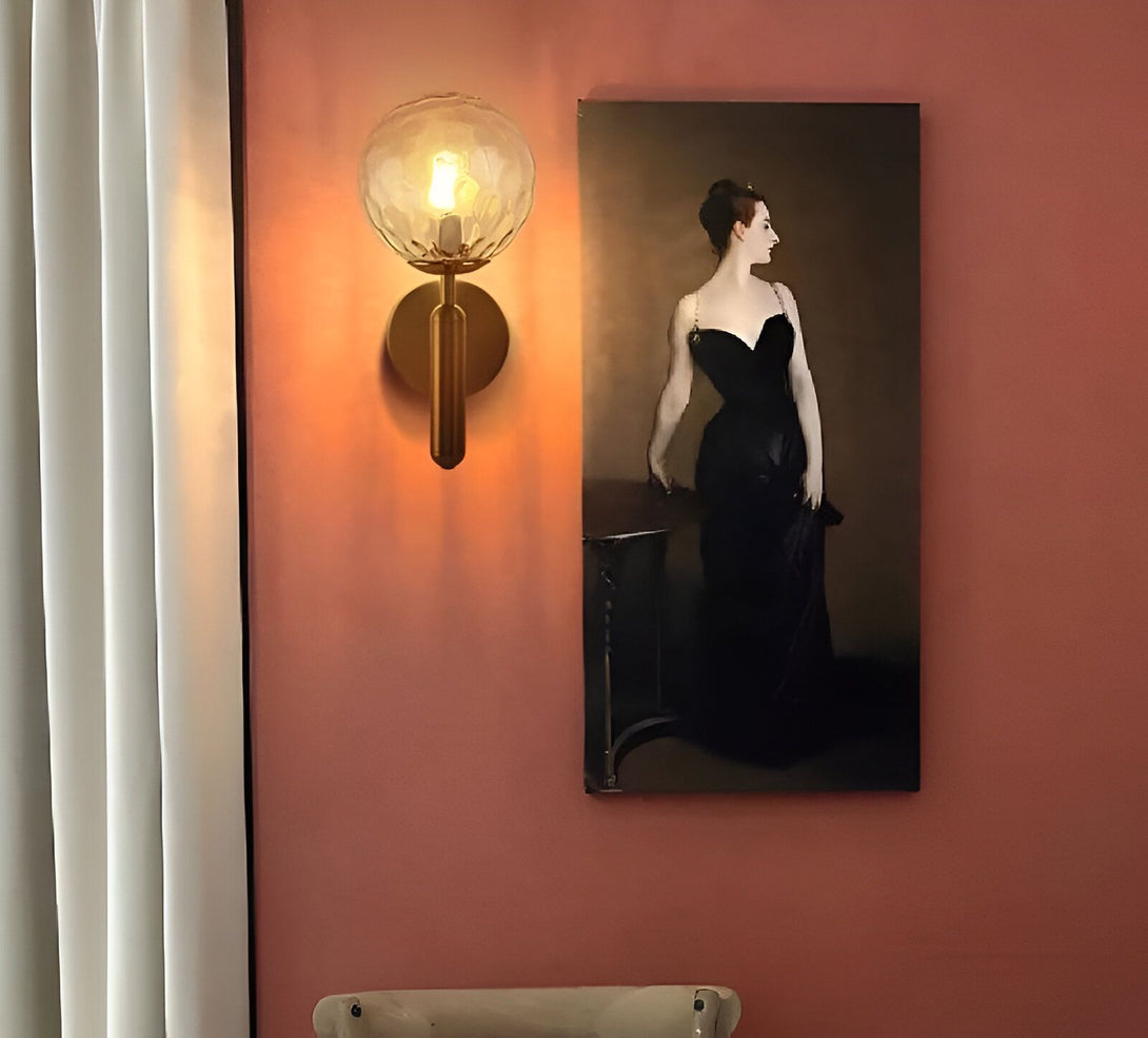 Une image d'une applique murale en laiton avec une boule en verre transparent. À côté de l'applique, il y a un tableau représentant une femme en robe noire. Le mur est peint en rose. HS-6642723279,