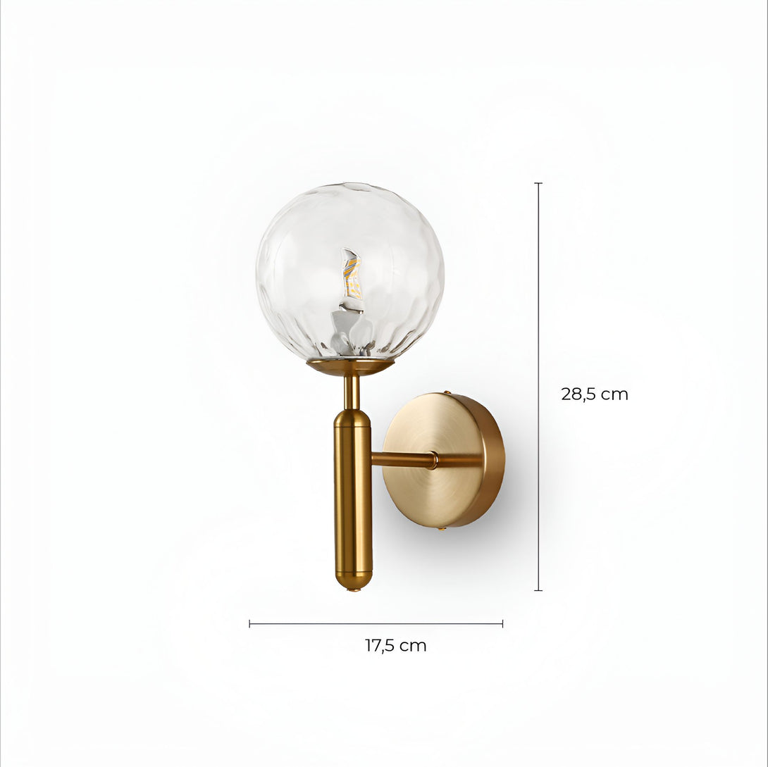 Une applique murale en laiton avec une sphère en verre transparent. La sphère en verre est soufflée à la bouche et présente un motif à bulles. L'applique murale est fixée au mur par une plaque ronde en laiton. L'ampoule est de type E14 et n'est pas incluse. L'applique murale mesure 17,5 cm de haut et 28,5 cm de large. HS-6642723279,