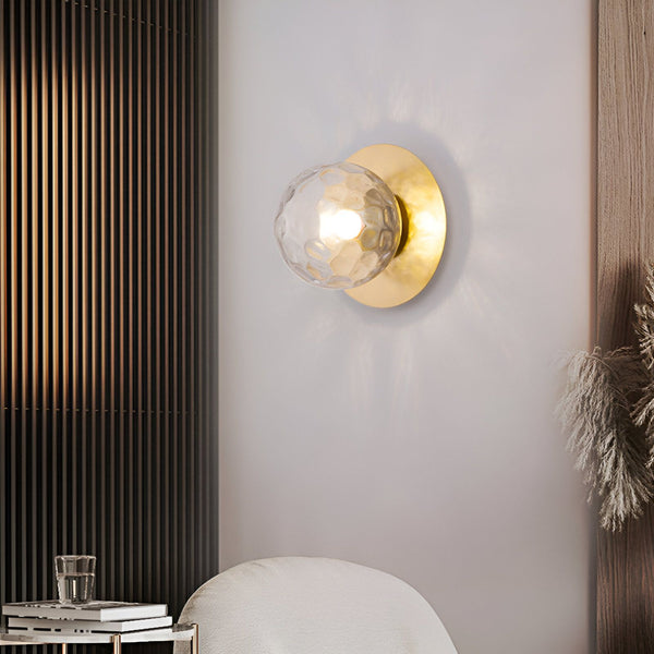 Une applique murale en forme de sphère en verre transparent avec des reflets dorés. La sphère est fixée à un support mural en métal doré. KE-2275189483,KE-5558580682,KE-7081243789,KE-0448745380,