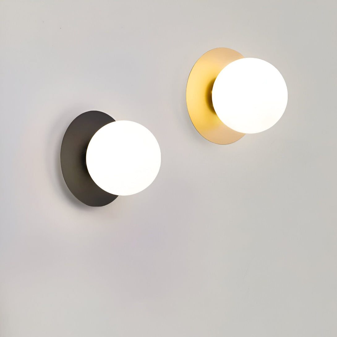 Deux appliques murales avec des abat-jour en verre blanc. L'applique murale de gauche a une base noire et l'applique murale de droite a une base dorée. KE-2275189483,KE-5558580682,KE-7081243789,KE-0448745380,