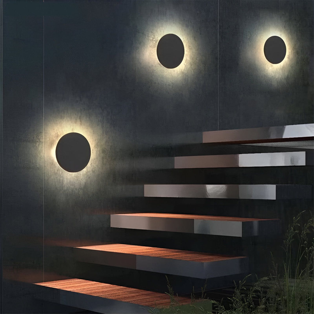 Trois appliques murales noires en forme de cercle sont fixées à un mur de béton brut. Les appliques sont disposées verticalement et éclairent le mur de haut en bas. LU-0937357146,LU-3212409584,LU-4507839009,LU-6078572369,