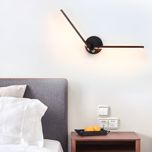 Une image d'une applique murale noire avec deux branches lumineuses. L'applique est fixée au mur au-dessus d'un lit avec une tête de lit grise. À côté du lit, il y a une table de chevet en bois avec un plateau noir عليها برتقال. DE-0021572577,DE-8803165533,DE-6581052280,DE-6471096585,DE-3704722901,DE-2437497684,DE-7739658669,DE-3646051795,