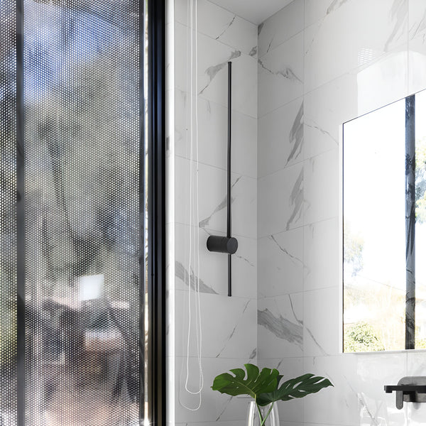 Une salle de bain avec un mur en marbre blanc et une paroi en verre dépoli. Il y a une douche avec un pommeau noir et un lavabo avec un robinet noir. Le sol est en marbre blanc. Il y a une plante verte dans un vase sur le lavabo. EM-4460156156,EM-9491391119,EM-7091335104,EM-2714779395,EM-6441388103,EM-2437079734,EM-5590103177,EM-2150536102,EM-957599227X,EM-8860104084,EM-8098031608,EM-5940573193,