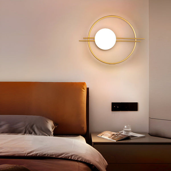 Une image d'une applique murale en métal doré avec une forme géométrique. L'applique est fixée au mur au-dessus d'un lit avec une tête de lit marron. HE-738953074X,HE-993358930X,HE-6888843173,HE-0002139596,HE-7137387454,HE-7408799672,