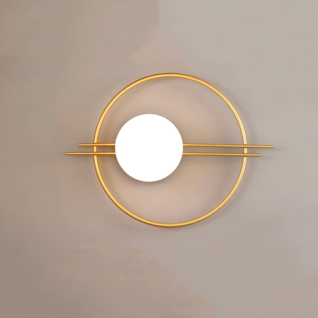Une applique murale en métal doré avec une forme ronde et une barre horizontale. L'applique est éclairée par une lumière LED blanche. HE-738953074X,HE-993358930X,HE-6888843173,HE-0002139596,HE-7137387454,HE-7408799672,
