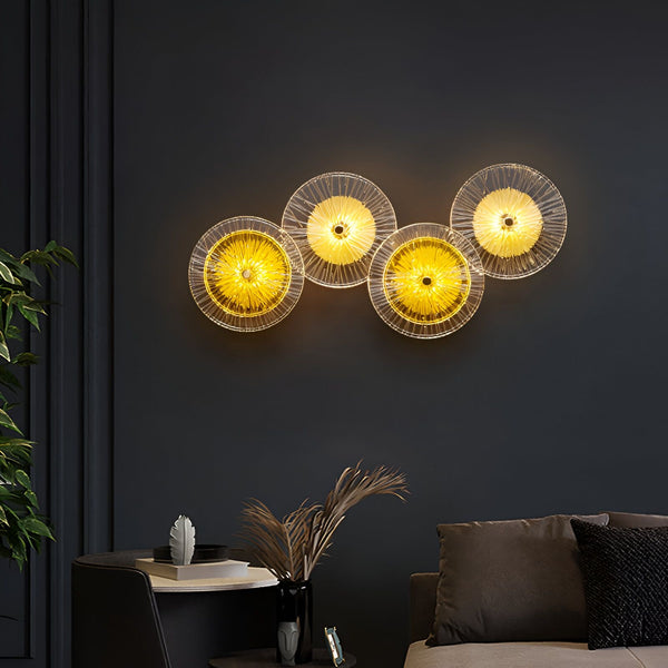 L'image représente une applique murale composée de quatre disques en verre transparent. Les disques sont disposés en ligne horizontale et sont éclairés par des LED. L'applique murale est fixée sur un mur peint en noir. AZ-1516305086,AZ-9770102490,