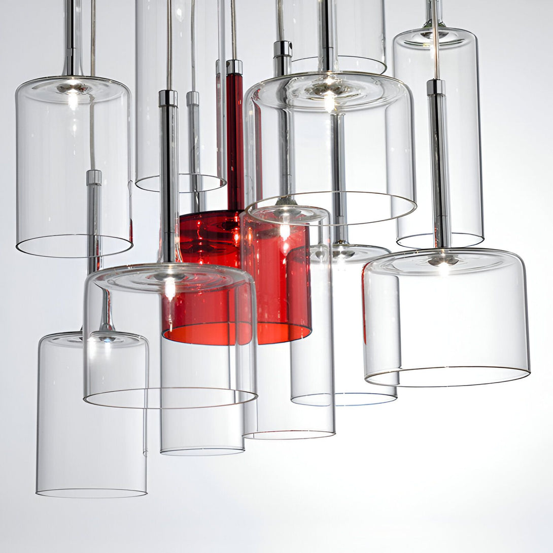 Une vue rapprochée d'une lampe suspendue industrielle. La lampe est composée de plusieurs tubes de verre transparents et d'un tube de verre rouge. Les tubes sont suspendus à des câbles métalliques.