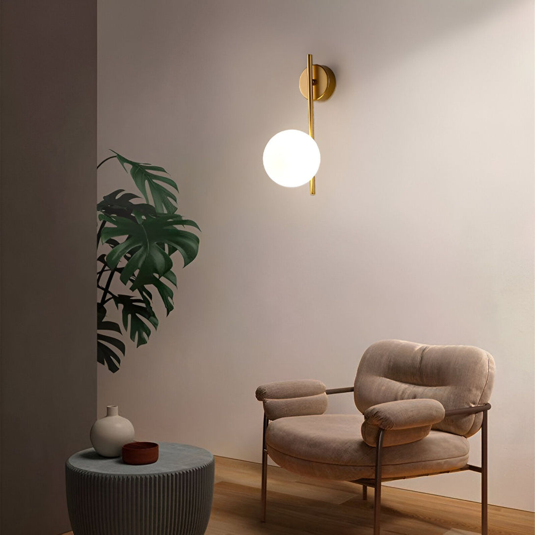 Une image d'une applique murale en laiton avec une boule en verre opale. L'applique est fixée au mur au-dessus d'un fauteuil en velours côtelé marron. À côté du fauteuil, il y a une table d'appoint avec un vase et une plante verte. GL-3736175507,GL-6321143758,GL-6843254969,GL-8040158036,GL-632193805X,GL-4001887061,GL-3434390774,GL-6755559571,
