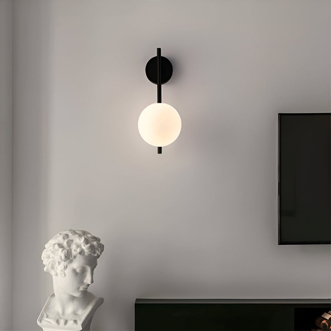 Une image d'une applique murale noire avec une boule en verre opale. L'applique est fixée au mur et diffuse une lumière douce et tamisée. À côté de l'applique, se trouve une sculpture en pierre blanche représentant une tête humaine. GL-3736175507,GL-6321143758,GL-6843254969,GL-8040158036,GL-632193805X,GL-4001887061,GL-3434390774,GL-6755559571,