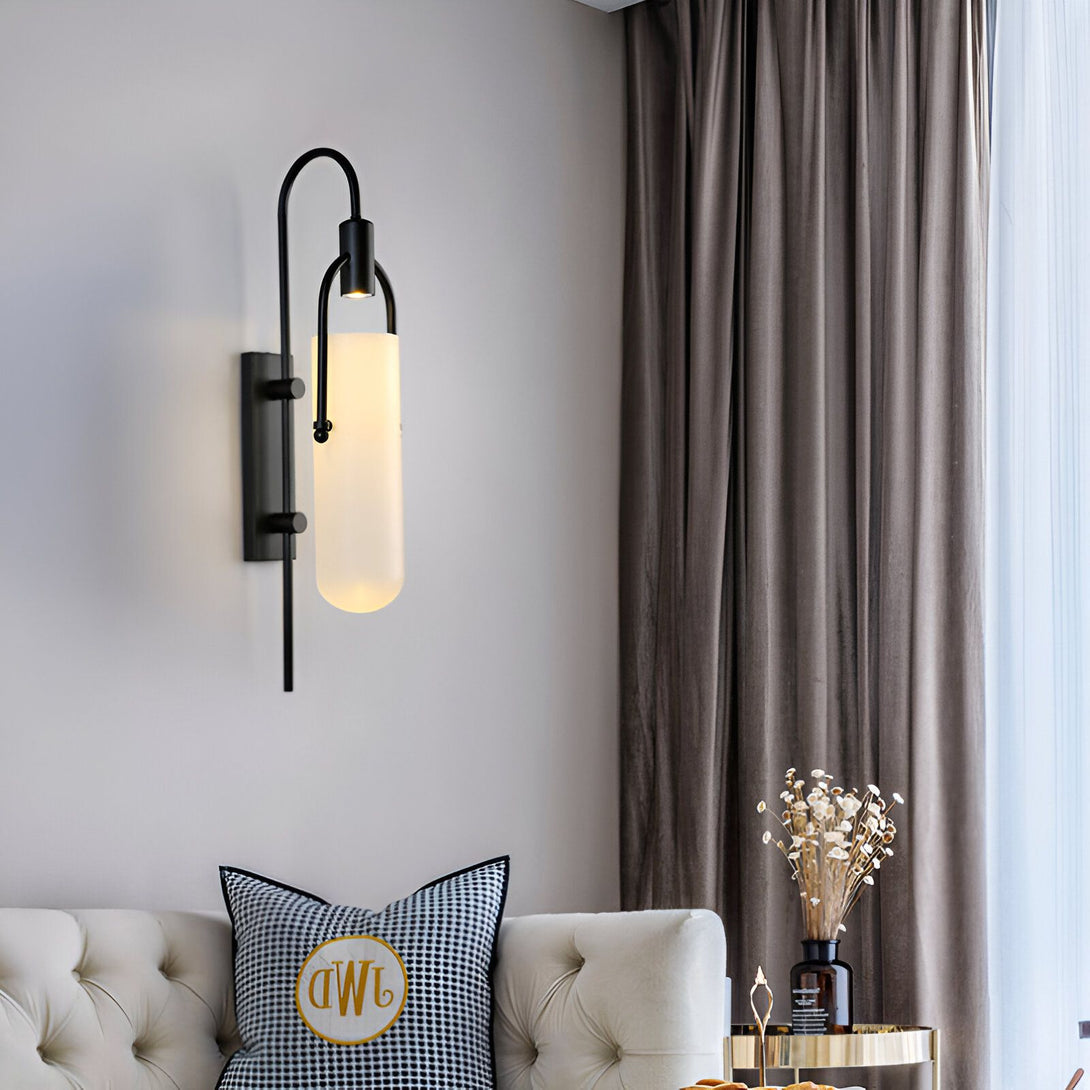 Une applique murale noire avec un abat-jour en verre opale. L'applique est fixée au mur au-dessus d'un canapé beige. ES-2484930887,ES-5612768230,ES-0022150080,ES-6055592797,ES-8057480351,ES-6019174972,ES-947368861X,ES-3587232709,