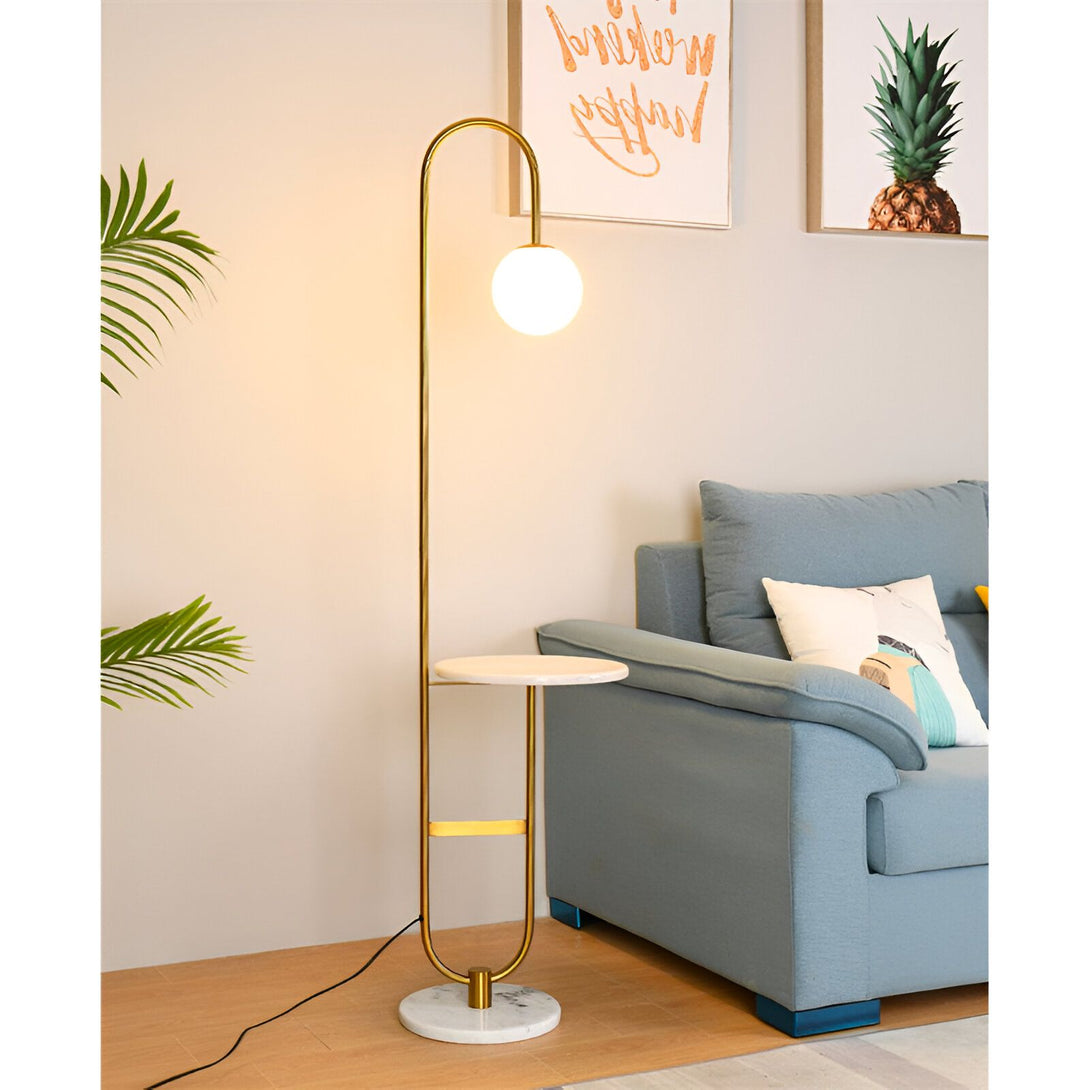 lampadaire doré avec une table intégrée en marbre blanc. À côté se trouve un canapé bleu avec des coussins blancs et une plante verte dans un pot. LA-5213525032,LA-9607473531,LA-1687313180,