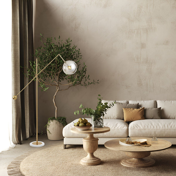 Une image d'un salon avec un canapé, une table basse, un lampadaire et un tapis. Le lampadaire est en métal doré et a un abat-jour en verre transparent. Le canapé est en tissu beige et a des coussins blancs et marron. La table basse est en bois et a un plateau rond. Le tapis est en jute et a une bordure marron. MA-3942036177,MA-3064936387,