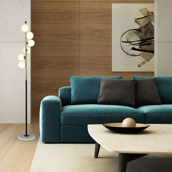 Un lampadaire doré avec cinq globes en verre opalin est placé à côté d'un canapé bleu foncé dans un salon. Le lampadaire est posé sur un tapis beige et le canapé est adossé à un mur en bois. Il y a une table basse en marbre avec un bol décoratif dessus. HS-6263847484,
