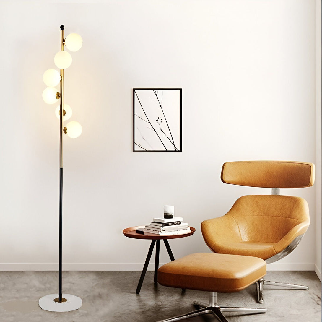 Un lampadaire noir avec des boules en verre doré. À côté se trouve un fauteuil marron et une table basse avec des livres dessus. HS-6263847484,