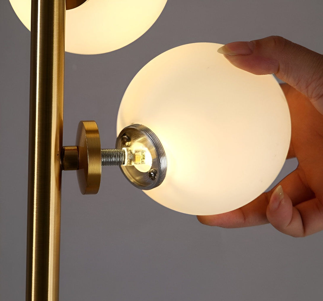 Une main visse une ampoule ronde en verre opalin sur un lampadaire doré. HS-6263847484,